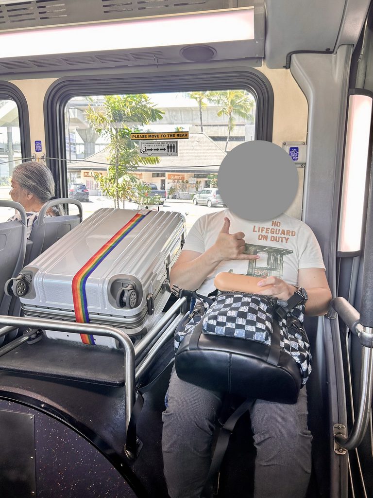 ハワイのWラインのバス車内で、荷物置き場にスーツケースを置いて座っているところ