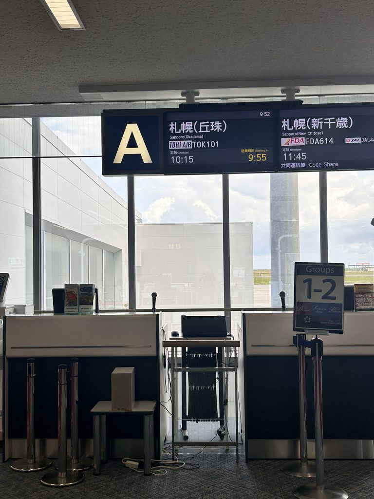 新潟空港の搭乗口A。案内板に、トキエアの札幌（丘珠）行き10:15発が表示されている