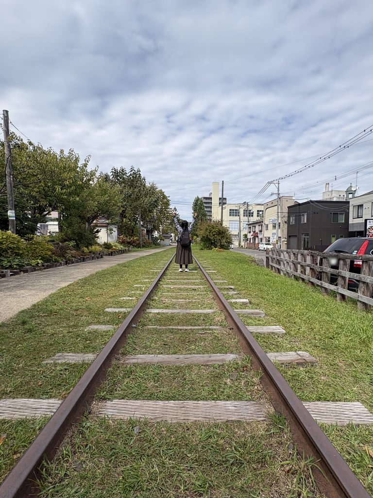 旧手宮線の線路の跡に、後ろ姿で両腕を上げて立つ私。草の生えた線路が奥へまっすぐ続いている