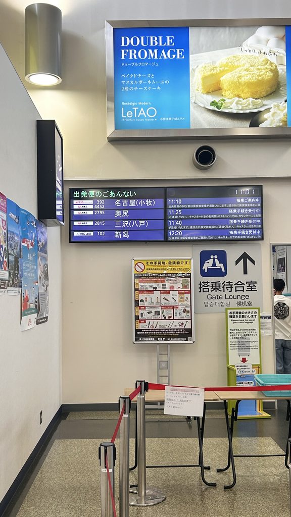 丘珠空港の搭乗待合室の入口と、出発便の案内板。トキエアの新潟行き12:20が表示されている